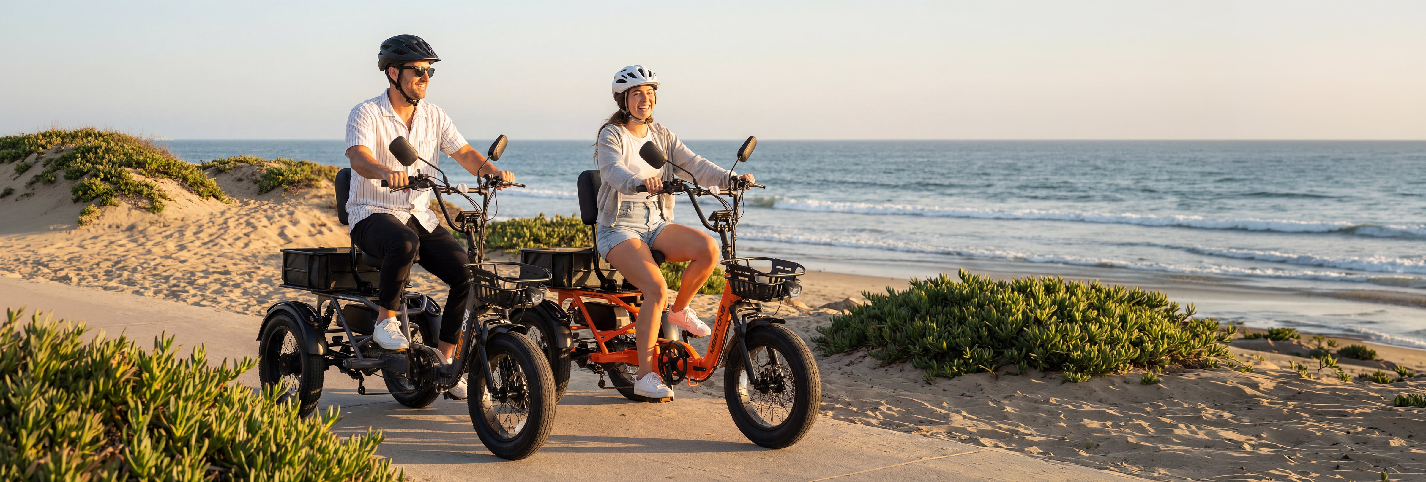 Two riders on Breeze Pro 2.0 electric trikes by the beach.